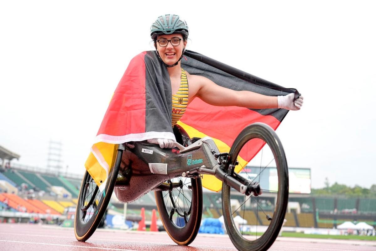 A female wheelchair racer celebrates on the track, holding the German flag